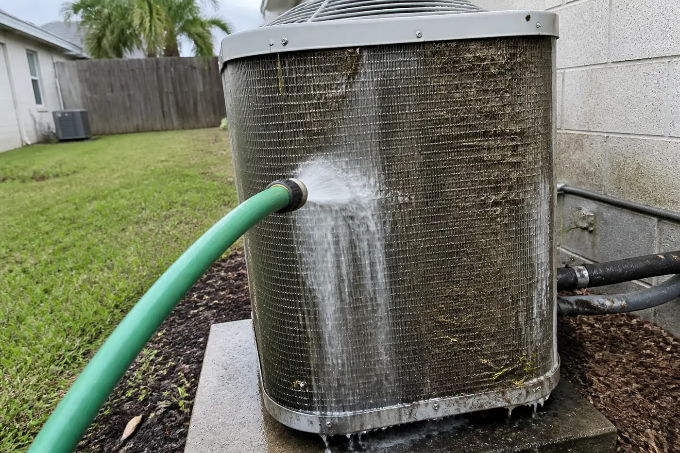 Outdoor AC condenser fins rinsed with a hose during AC maintenance in Tampa