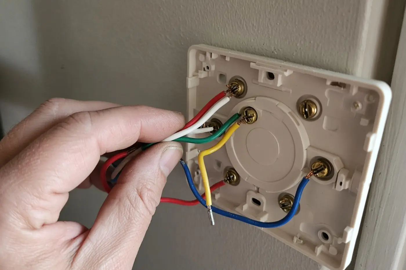 Hands landing thermostat wires on a wall subbase during smart thermostat installation in Tampa